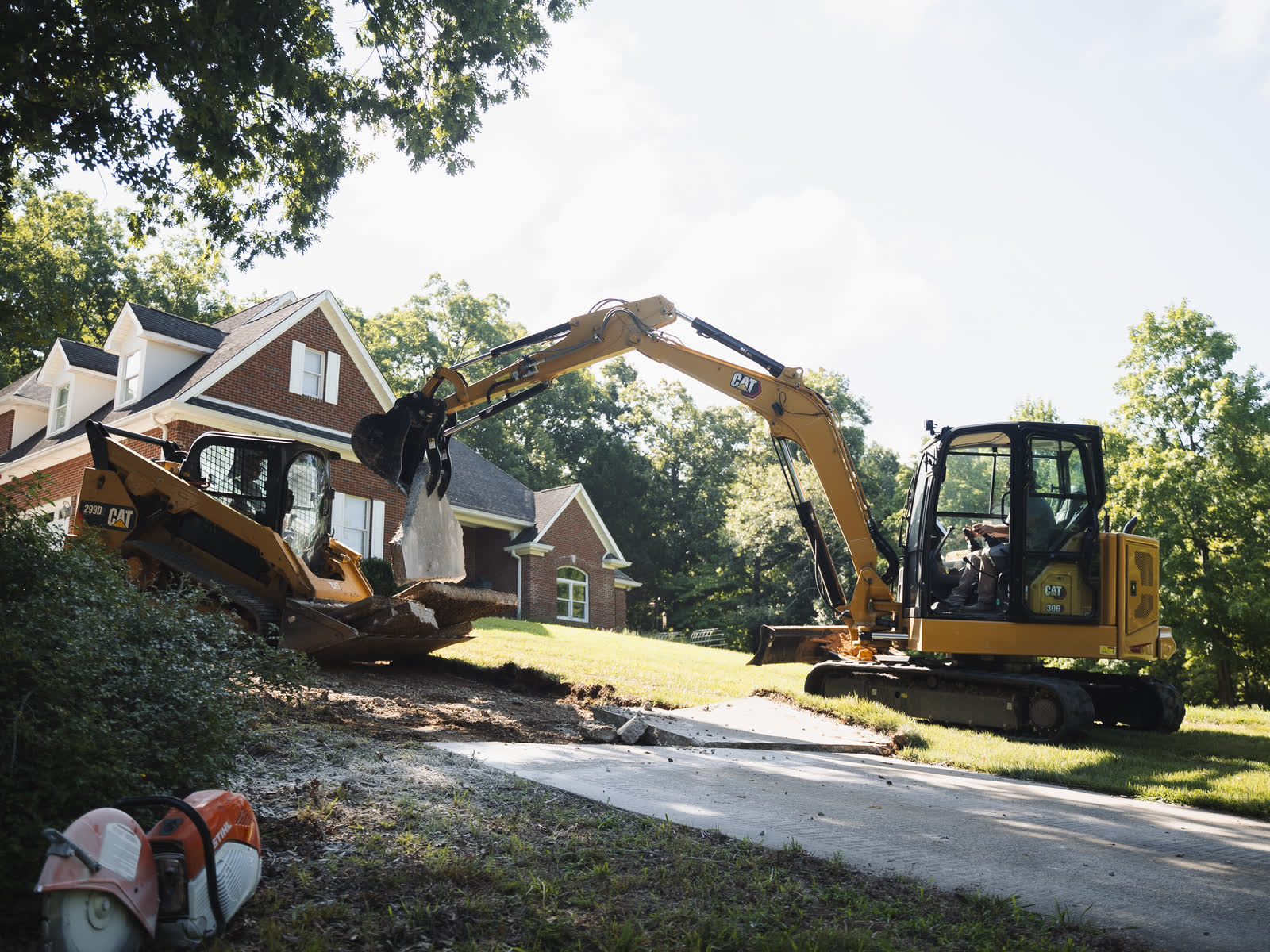 Excavator and skid steer breaking out a cracked concrete driveway at a brick home in Chattanooga, TN